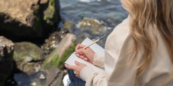 5 Ways To Switch Your Strength and Flexibility Mindset - women writing in her journal sitting on a lake