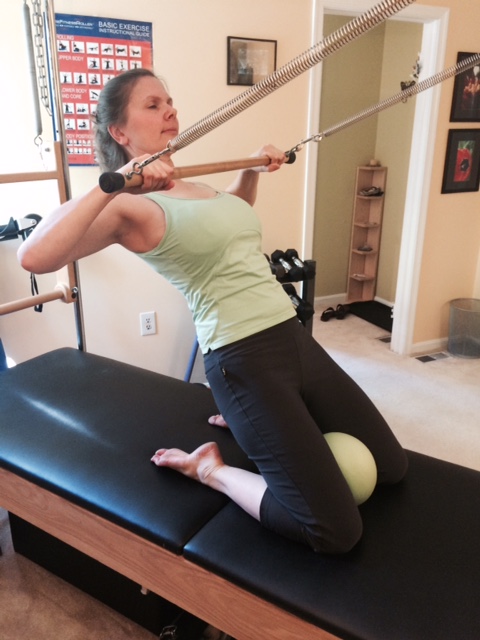 Woman over 50 working out on the Pilates Cadillac in her in-person session at the HEYlifetraining studio.