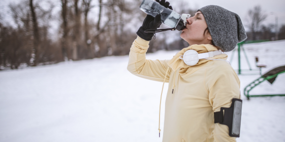 woman drinking water outside in snow