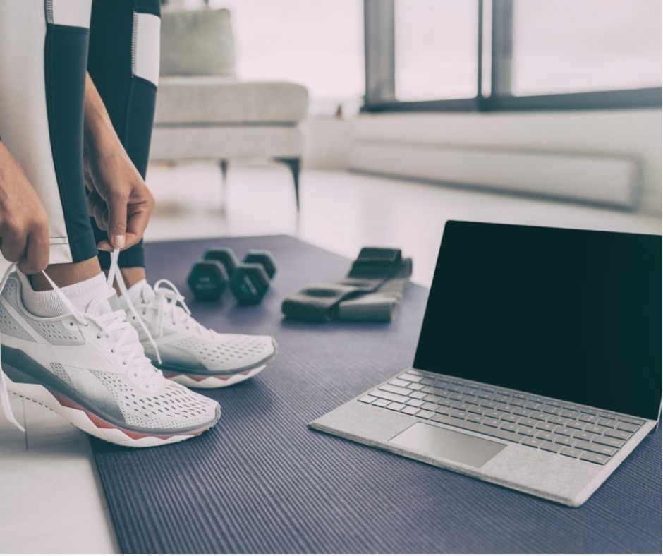 Person tying shoes next to a lap top and weights, online fitness and nutrition coaching.