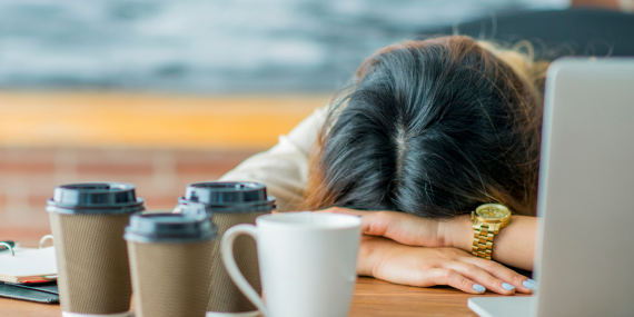 woman sleeping at her desk with several cups of coffee and feel the midlife fatigue