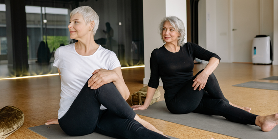 Fitness After 50: Why Your Body Feels Different. two women doing a yoga twist on the floor